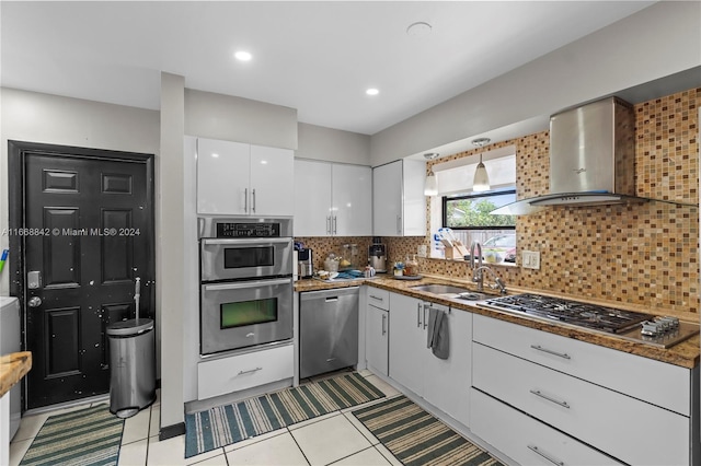 kitchen with white cabinets, light tile patterned floors, wall chimney range hood, appliances with stainless steel finishes, and decorative backsplash