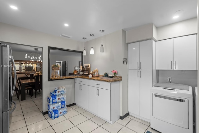 kitchen with white cabinetry, stainless steel refrigerator, washer / dryer, decorative light fixtures, and dark stone counters