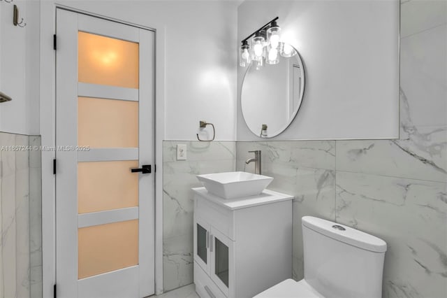 bathroom featuring toilet, marble finish floor, tile walls, and vanity