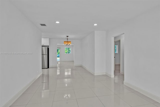 empty room featuring visible vents, a notable chandelier, baseboards, and light tile patterned flooring