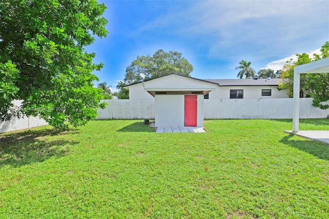 rear view of property with a lawn, an outdoor structure, and a fenced backyard