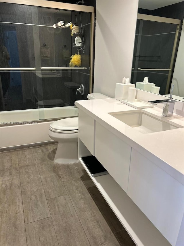 full bathroom with wood-type flooring, shower / bath combination with glass door, vanity, and toilet