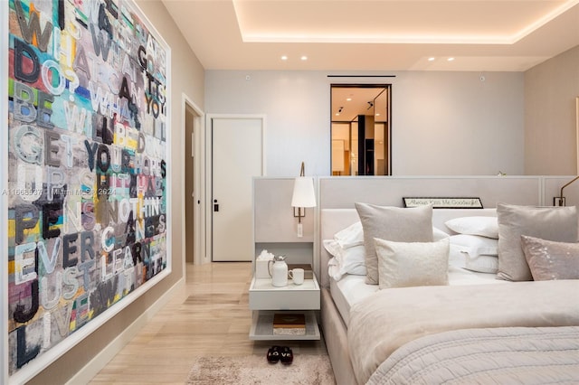 bedroom with light wood-type flooring and a raised ceiling