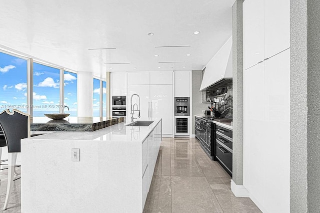 kitchen featuring a water view, a wall of windows, sink, white cabinets, and a large island