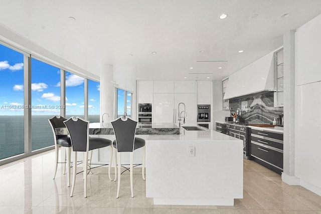 kitchen with a water view, a kitchen island with sink, decorative backsplash, white cabinets, and a kitchen bar