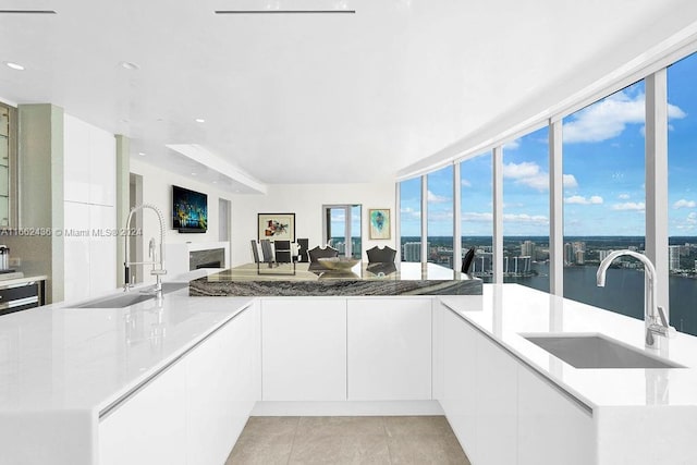 kitchen with white cabinets, light tile patterned flooring, light stone countertops, and sink