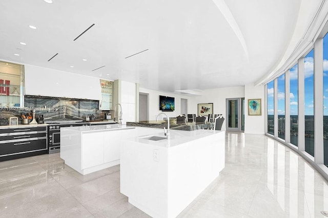 kitchen with a center island with sink, white cabinetry, sink, and tasteful backsplash