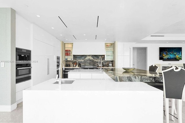 kitchen featuring tasteful backsplash, white cabinets, sink, stainless steel oven, and a spacious island