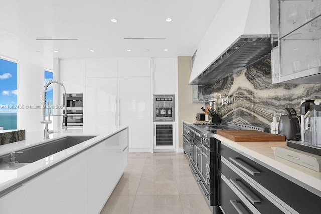 kitchen featuring tasteful backsplash, white cabinets, sink, extractor fan, and high end stainless steel range