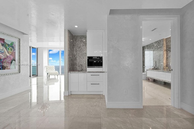 kitchen featuring light stone counters, stainless steel oven, and white cabinetry