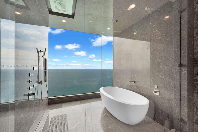 bathroom with a water view, tile patterned floors, tile walls, and a washtub