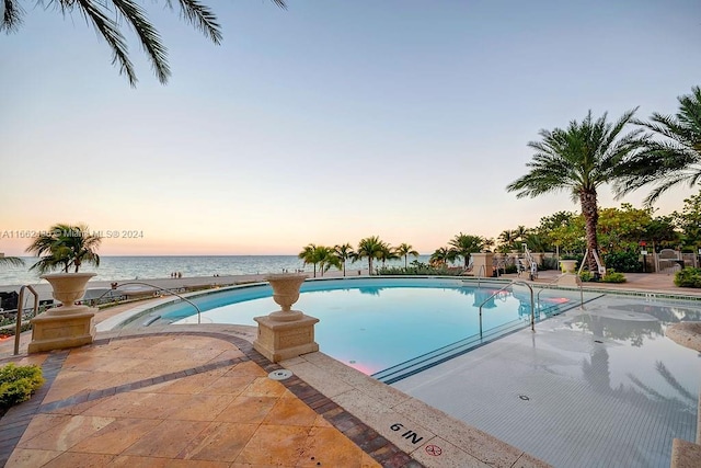 pool at dusk with a water view and a patio