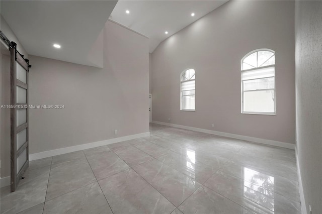 spare room with light tile patterned flooring, a barn door, and high vaulted ceiling