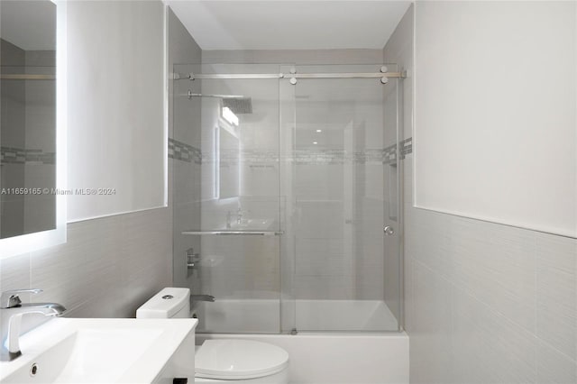 full bathroom with vanity, tile walls, toilet, and combined bath / shower with glass door