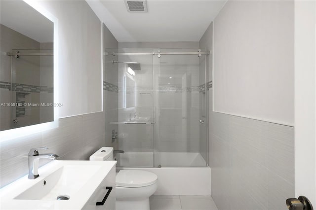 full bathroom with tile walls, tile patterned flooring, shower / bath combination with glass door, vanity, and toilet