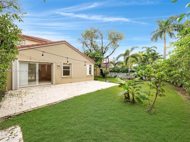 rear view of house with stucco siding, fence, a lawn, and a patio area