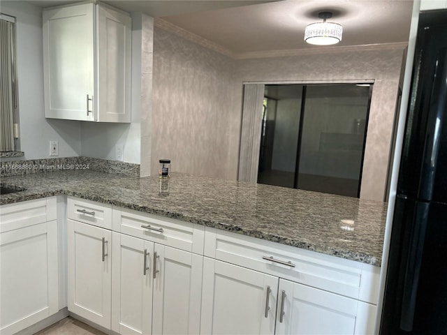 kitchen with black refrigerator, crown molding, dark stone countertops, and white cabinets