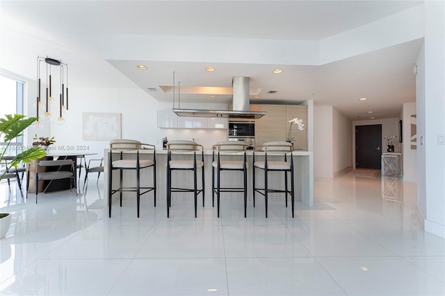 kitchen featuring a breakfast bar, island range hood, light tile patterned floors, black oven, and decorative light fixtures