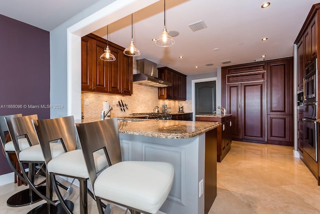 kitchen featuring decorative backsplash, light stone counters, wall chimney exhaust hood, kitchen peninsula, and pendant lighting