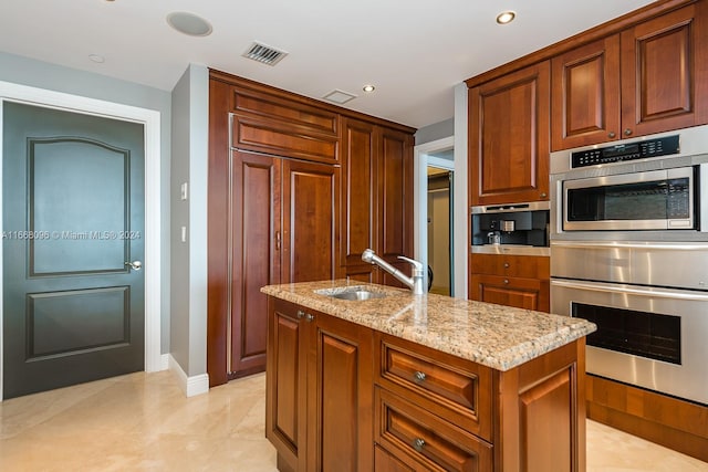 kitchen with light tile patterned flooring, light stone counters, a center island with sink, double oven, and sink