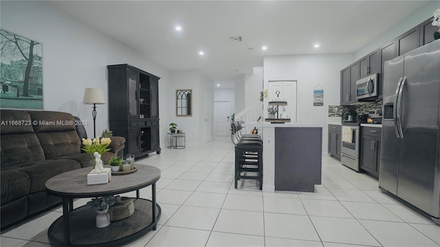 kitchen featuring a center island, a breakfast bar area, backsplash, appliances with stainless steel finishes, and light tile patterned floors