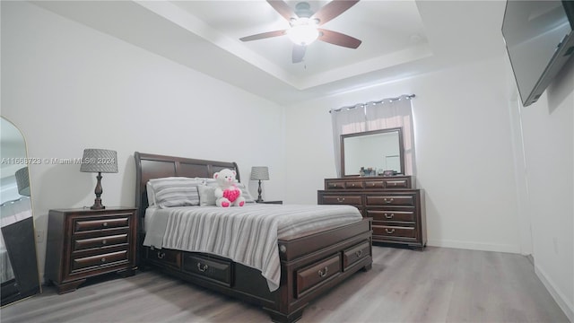 bedroom with ceiling fan, light wood-type flooring, and a raised ceiling