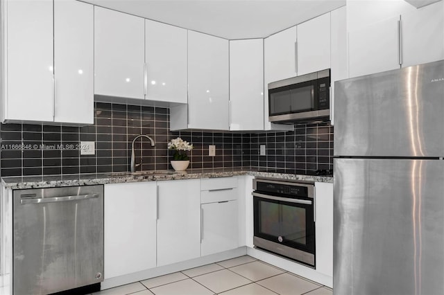 kitchen featuring white cabinetry, backsplash, appliances with stainless steel finishes, and dark stone counters