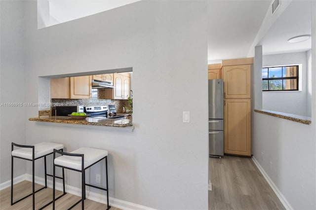 kitchen with light wood-type flooring, decorative backsplash, light brown cabinetry, and stainless steel appliances