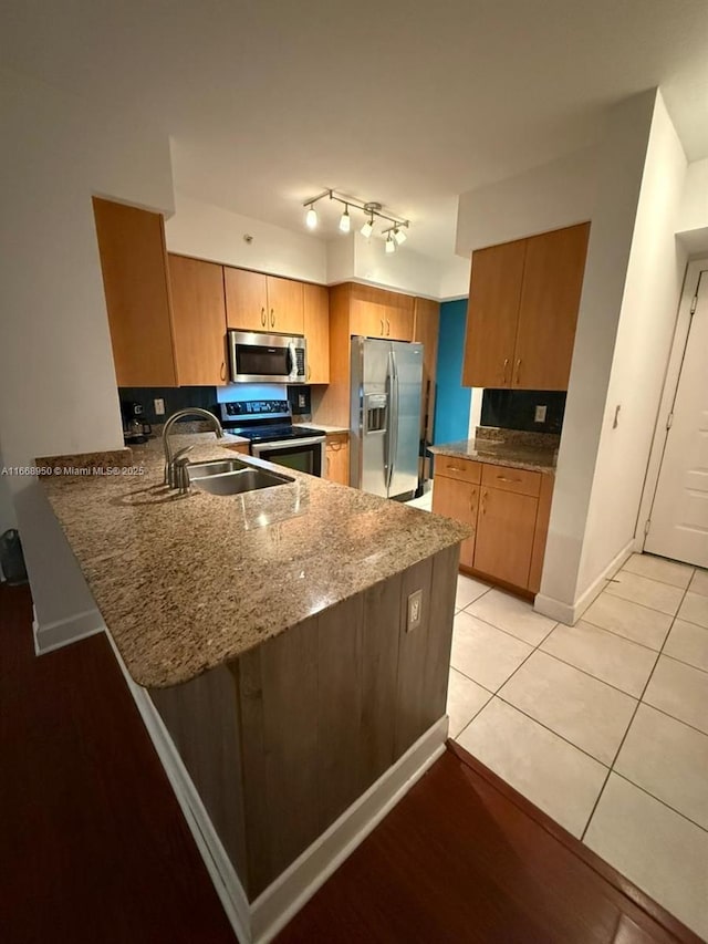 kitchen with light stone countertops, sink, kitchen peninsula, light tile patterned floors, and appliances with stainless steel finishes