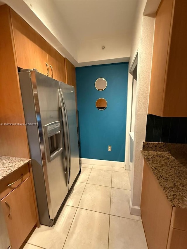 kitchen featuring light tile patterned flooring, light stone countertops, and stainless steel fridge with ice dispenser