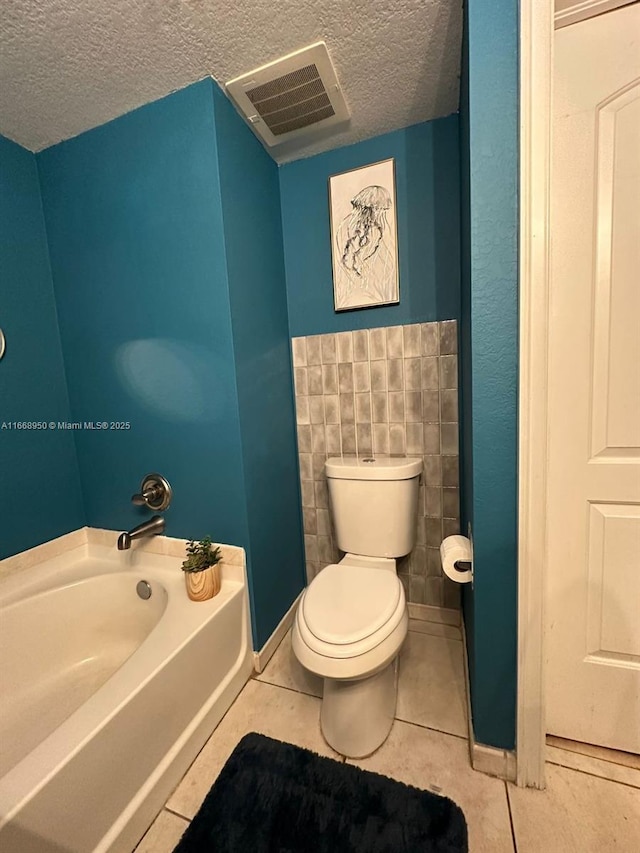 bathroom with tile patterned floors, a tub to relax in, a textured ceiling, and toilet