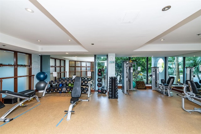 workout area with a raised ceiling, recessed lighting, and expansive windows