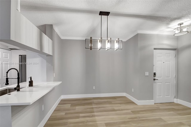 kitchen featuring a textured ceiling, decorative light fixtures, crown molding, and light hardwood / wood-style floors