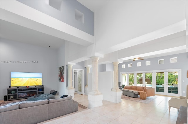 tiled living room featuring french doors, a towering ceiling, decorative columns, and ceiling fan