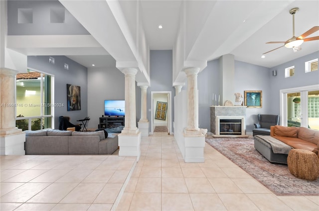 living room with ceiling fan, light tile patterned floors, a high end fireplace, high vaulted ceiling, and ornate columns