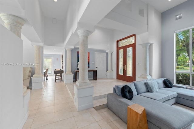 living room featuring french doors, light tile patterned floors, a towering ceiling, and decorative columns