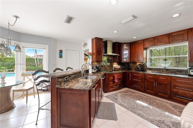 kitchen featuring hanging light fixtures, sink, wall chimney exhaust hood, a breakfast bar area, and decorative backsplash