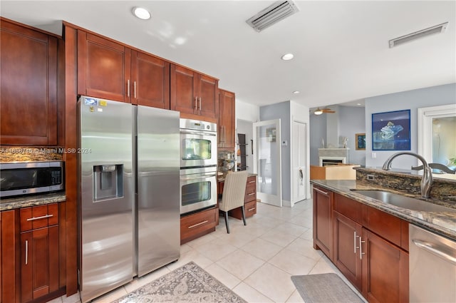 kitchen with dark stone countertops, light tile patterned flooring, sink, and stainless steel appliances