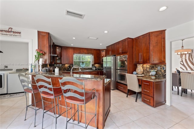 kitchen with dark stone countertops, tasteful backsplash, washer and dryer, and stainless steel appliances