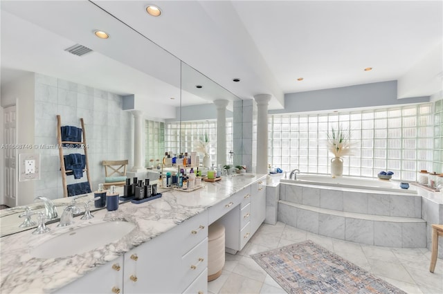 bathroom featuring decorative columns, vanity, and a relaxing tiled tub