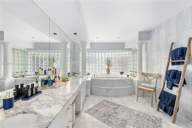 bathroom featuring tile walls, vanity, a relaxing tiled tub, and ornate columns