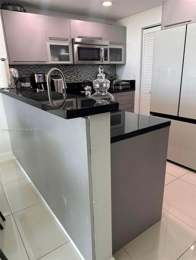 kitchen with backsplash, kitchen peninsula, light tile patterned flooring, and stainless steel appliances