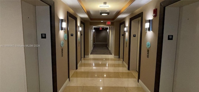 hallway featuring a raised ceiling, light tile patterned flooring, and elevator