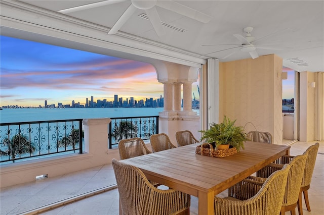 balcony at dusk featuring a water view and ceiling fan