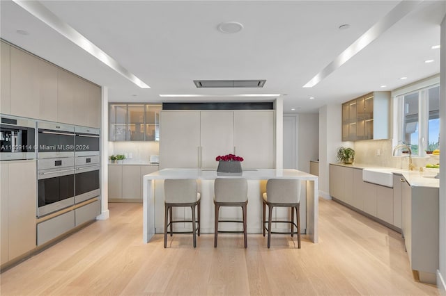 kitchen featuring light wood-type flooring, a center island, a breakfast bar area, sink, and gray cabinetry