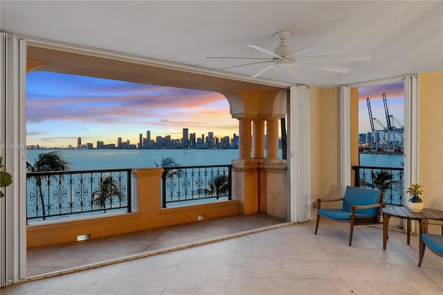 patio terrace at dusk with a water view, ceiling fan, and a balcony