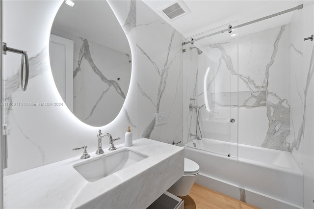 full bathroom with wood-type flooring, combined bath / shower with glass door, sink, and toilet