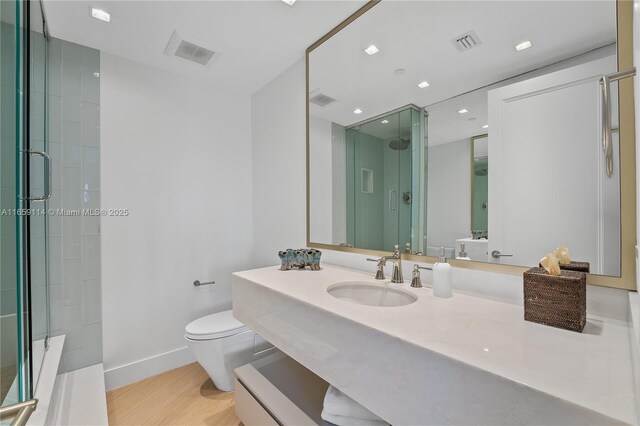 bathroom featuring wood-type flooring, toilet, a shower with shower door, and sink