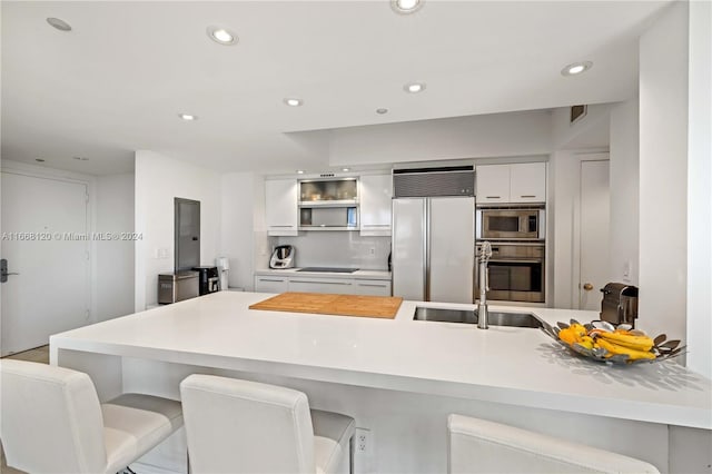 kitchen with white cabinets, a kitchen bar, black electric stovetop, sink, and paneled fridge