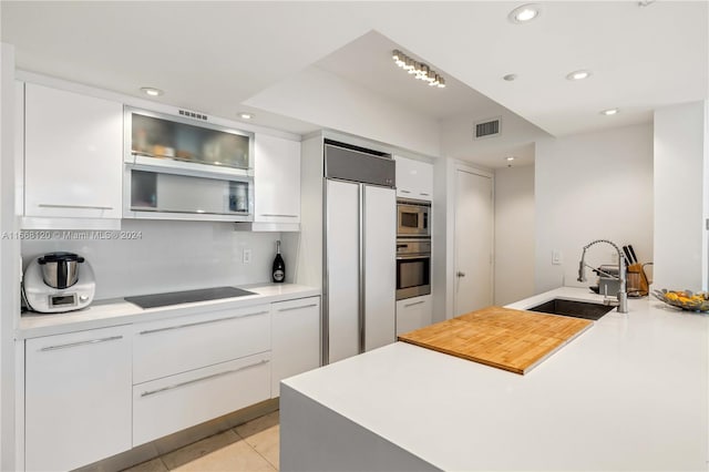 kitchen with white cabinetry, light tile patterned floors, built in appliances, and sink